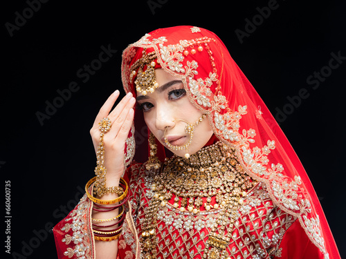 Headshot portrait of a beautiful Asian Muslim lady in a hijab wearing a gorgeous Bollywood or Indian themed red traditional wedding dress isolated on dark background