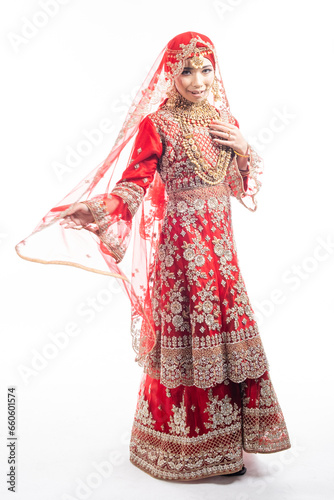 Full height portrait of a beautiful Asian Muslim lady in a hijab wearing a gorgeous Bollywood or Indian themed red traditional wedding dress isolated on white background