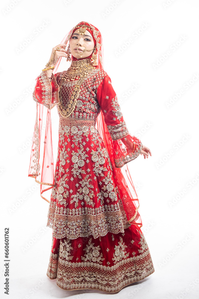 Full height portrait of a beautiful Asian Muslim lady in a hijab wearing a gorgeous Bollywood or Indian themed red traditional wedding dress isolated on white background