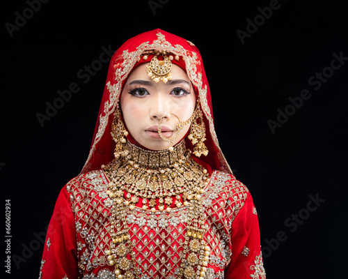 Close up portrait of a beautiful Asian Muslim lady in a hijab wearing a gorgeous Bollywood or Indian themed red traditional wedding dress isolated on dark background © HEMINXYLAN