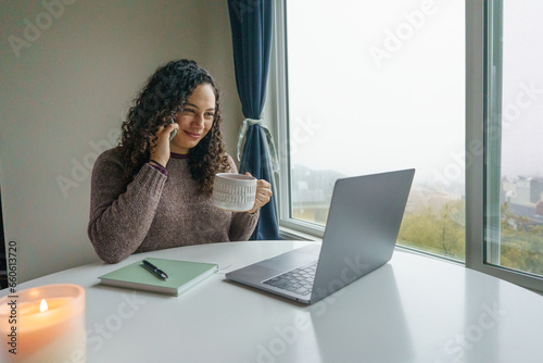 Curly hair young woman working on laptop in cozy nook with mug	