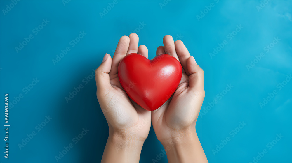 Fototapeta premium Hands holding a red heart on a blue background, heart donation promotion concept