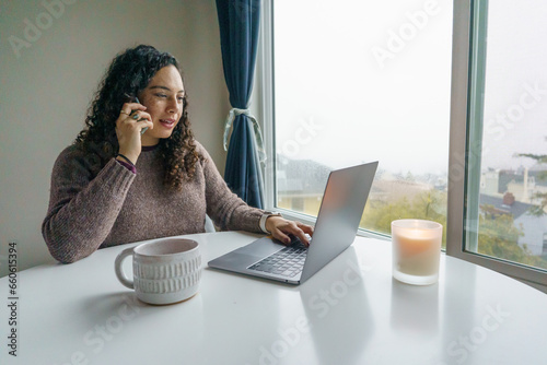 Curly hair young woman working on laptop in cozy nook with mug	