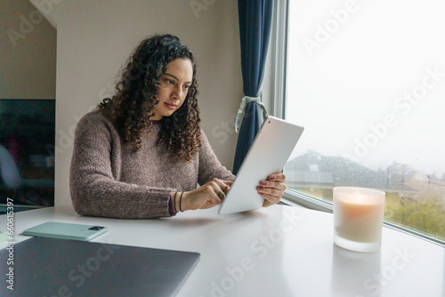Curly hair young woman working on laptop in cozy nook with mug	