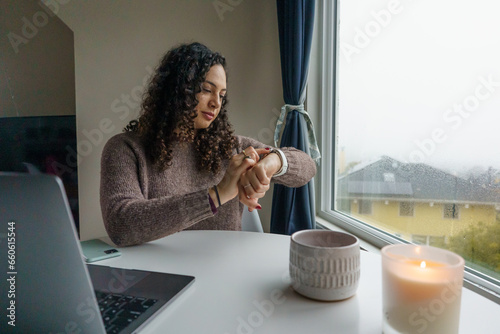 Curly hair young woman working on laptop in cozy nook with mug	