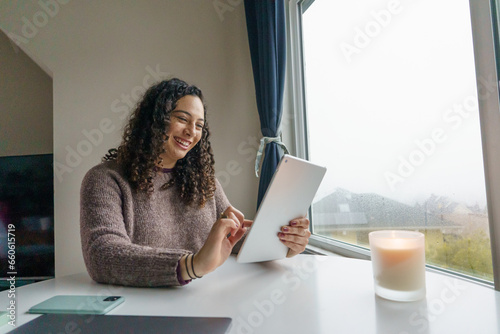 Curly hair young woman working on laptop in cozy nook with mug	