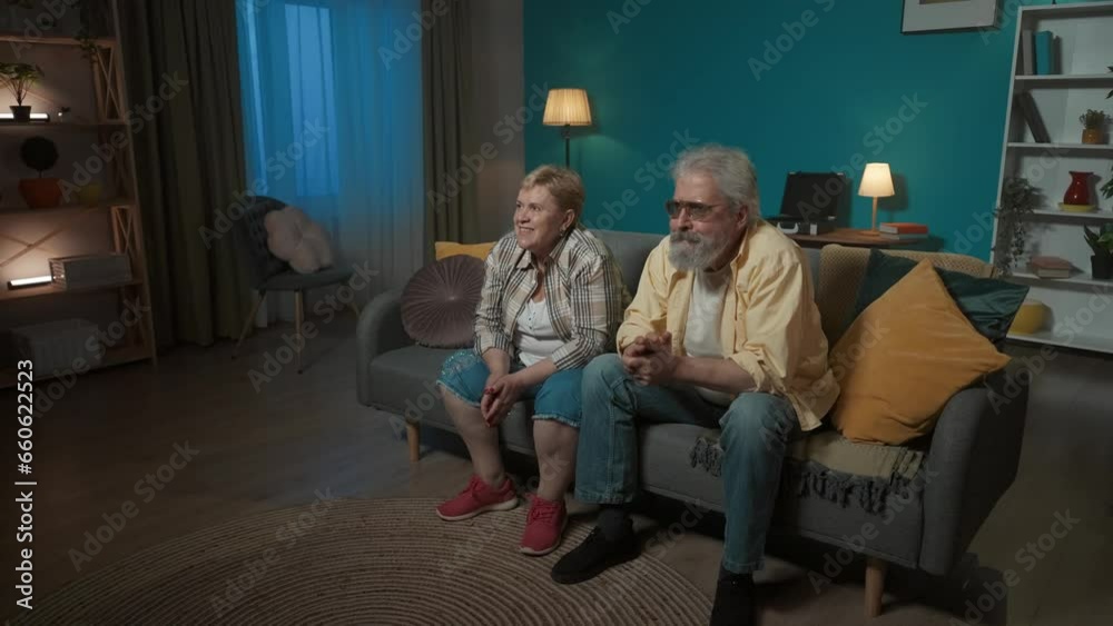 Elderly couple sitting on a couch in a room, staring intently somewhere. They feel excitement, they are waiting for something. Then they get upset, they get angry. Demonstrating sadness, sorrow. Elderly couple sitting on a couch in a room, staring intently somewhere. They feel excitement, they are waiting for something. Then they get upset, they get angry. Demonstrating sadness, sorrow.