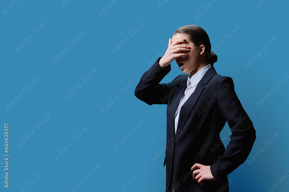 Shocked teenage girl looking at copy space, blue studio background, covering face with hands Shocked teenage girl looking at copy space, blue studio background, covering face with hands