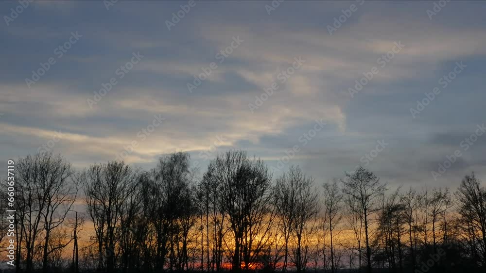 Evening sky with red and orange sunset, moving clouds and horizon with dark winter trees moved by wind on windy day - timelapse. Topics: weather, meteorology, season, dusk, natural environment Evening sky with red and orange sunset, moving clouds and horizon with dark winter trees moved by wind on windy day - timelapse. Topics: weather, meteorology, season, dusk, natural environment