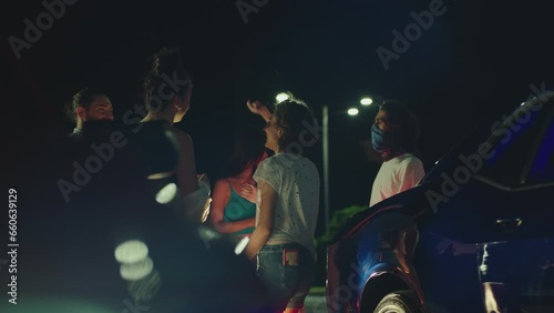 Group of young people dancing near muscle car . Crowd of stylish fans having fan during car races . Young people partying in outdoors at night. Competition of Beautiful american sport cars Slow motion