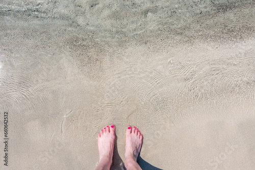 Detail of female feet with pink nail polish on a beautiful beach with pink sand and crystal clear water. Longing for the sea, freedom and summer. Shot in the beautiful pink beach of Elafonissi.