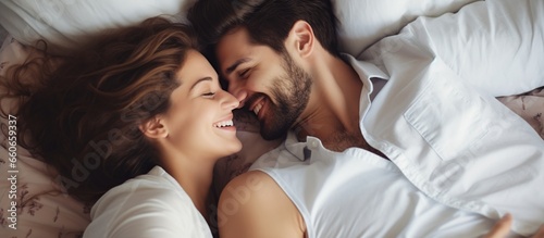 Young loving couple lying in bed laughing and smiling with blanket.