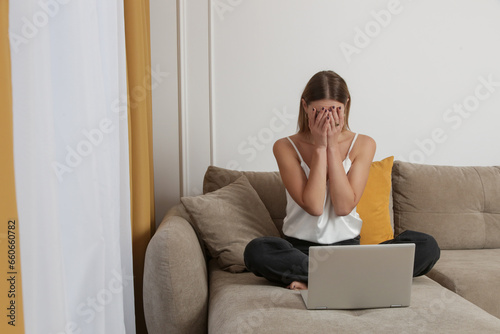 Portrait of young worried, depressed woman working from home. Writer, blogger, freelancer or student covering face with hands in front of laptop, Woman under the pressure, receiving bad news. photo