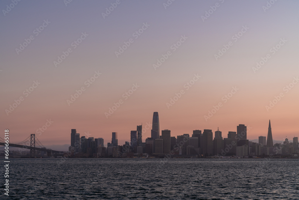 A picturesque skyline of San Francisco Panorama at sunset golden hour from Treasure Island, California, United States. Panoramic view of cityscape with mist and foggy air. Illuminated dusk city