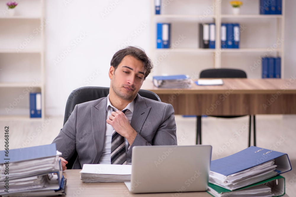 Young male employee unhappy with excessive work in the office Young male employee unhappy with excessive work in the office