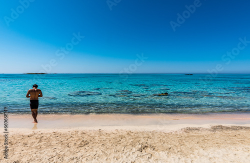 Black boy by the sea. Spectacular panorama of Elafonissi Beach in Crete with Turquoise Water and the famous pink sand. The man is wearing a swimsuit and is sunny-side up.