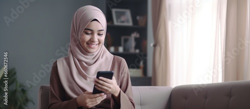 Beautiful Muslim woman playing with cellphone sitting on sofa chair