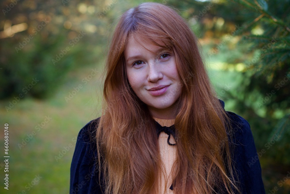 Fototapeta premium Witch young ginger woman in a black robe walks through the forest, the concept of Halloween, esotericism, mysticism, magic, sorcery, pumpkin