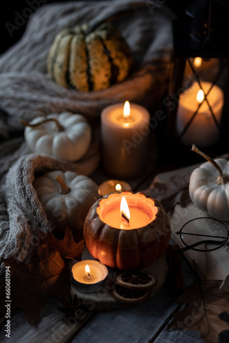 Atmospheric candle - shape of pumpkins  autumn decor  book on grey fall rainy day. Autumn cozy home atmosphere  inspiration  hygge concept. Aromatherapy  warming  relaxation. Wooden background