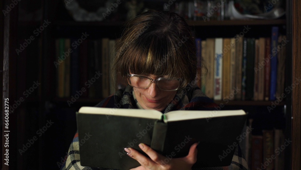A woman is reading a book, there are many books in the background. In funny glasses, he studies literature at home. A smart girl holds a book in her hands. Studying at night, close-up in retro style. A woman is reading a book, there are many books in the background. In funny glasses, he studies literature at home. A smart girl holds a book in her hands. Studying at night, close-up in retro style.