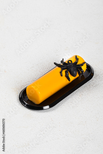 Themed pumpkin cream dessert bar decorated with spider jelly on a black serving plate. White gray background. Close up. Halloween