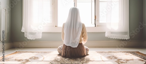 young muslim woman in hijab praying indoors near the window photo