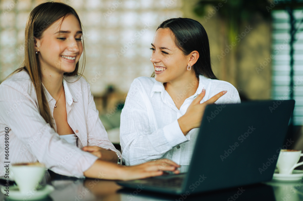 Two happy female friends are sitting in a coffee shop and searching the internet