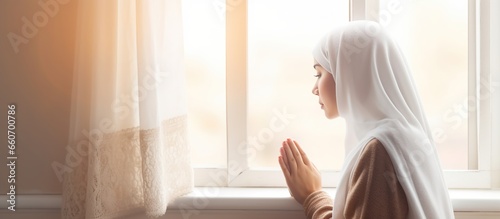 Muslim woman in hijab praying indoors near the window