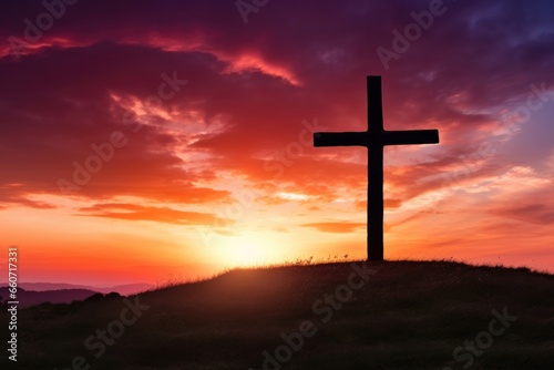 A breathtaking scene of a cross, standing atop a grassy hill, silhouetted against a stunning sunset that fills the sky with shades of red, orange, and purple.