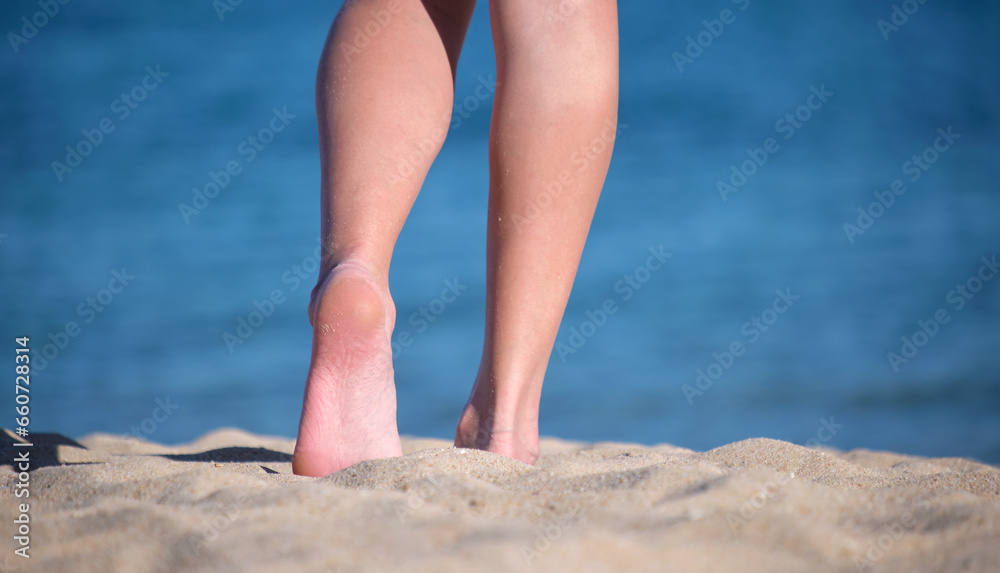 Close up of female feet walking barefoot on white grainy sand of golden beach on blue ocean water background Close up of female feet walking barefoot on white grainy sand of golden beach on blue ocean water background
