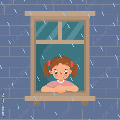 Cute little girl looking at raindrops from window feeling sad can not play outside