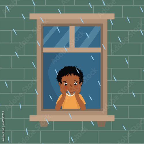 Cute little African boy looking at raindrops from window feeling sad can not play outside