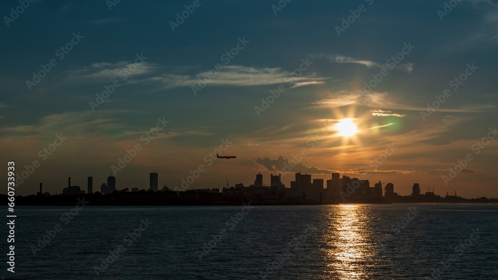Silhouette of Boston from Boston Harbor with an airplane coming in for a landing