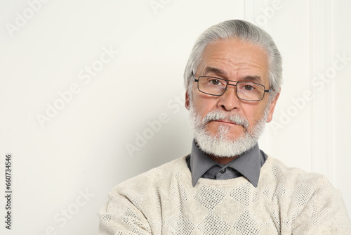 Portrait of handsome senior man in eyeglasses near white wall. Space for text