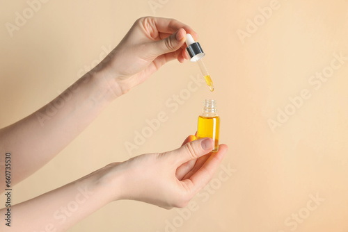 Woman holding bottle of cosmetic oil on beige background, closeup