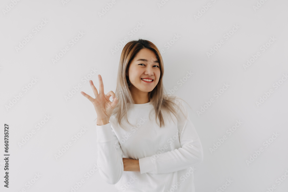 Asian Thai woman smiling and showing okay sign gesture, giving positive feedback, isolated on white background in winter. Asian Thai woman smiling and showing okay sign gesture, giving positive feedback, isolated on white background in winter.