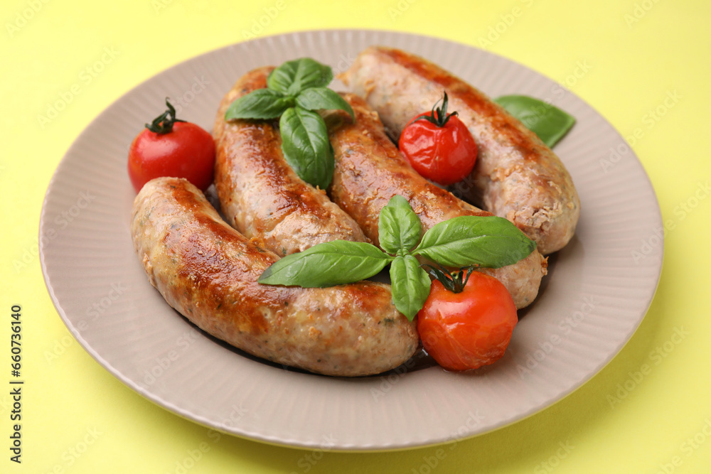Plate with tasty homemade sausages, basil leaves and tomatoes on yellow table, closeup