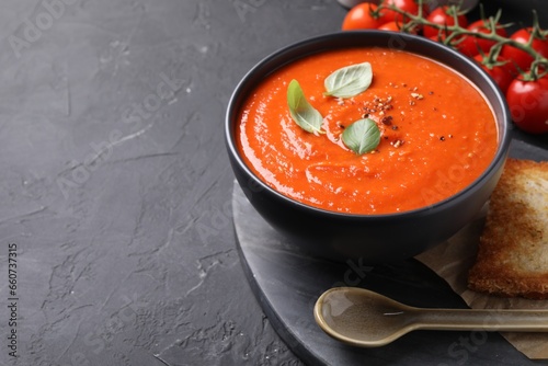 Delicious tomato cream soup served on black textured table. Space for text