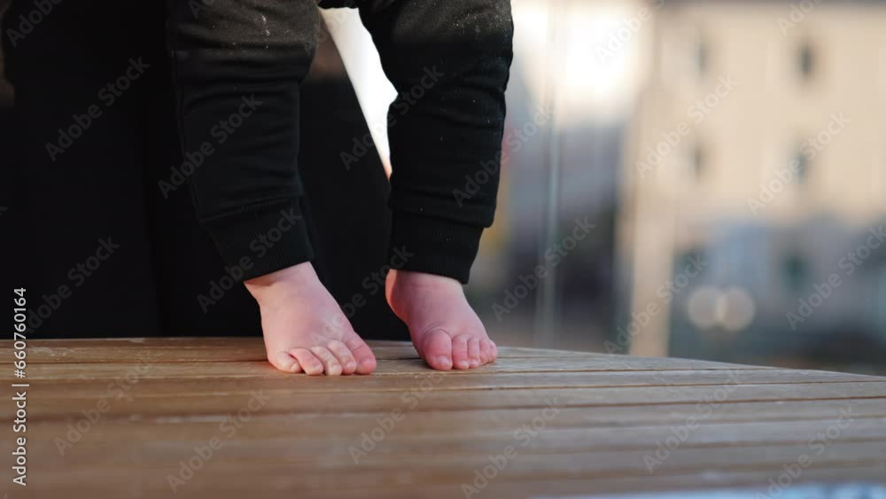 Tiny bare feet of a baby on the wooden surface. Kid wearing black pants stepping by the table. Blurred backdrop. Tiny bare feet of a baby on the wooden surface. Kid wearing black pants stepping by the table. Blurred backdrop.