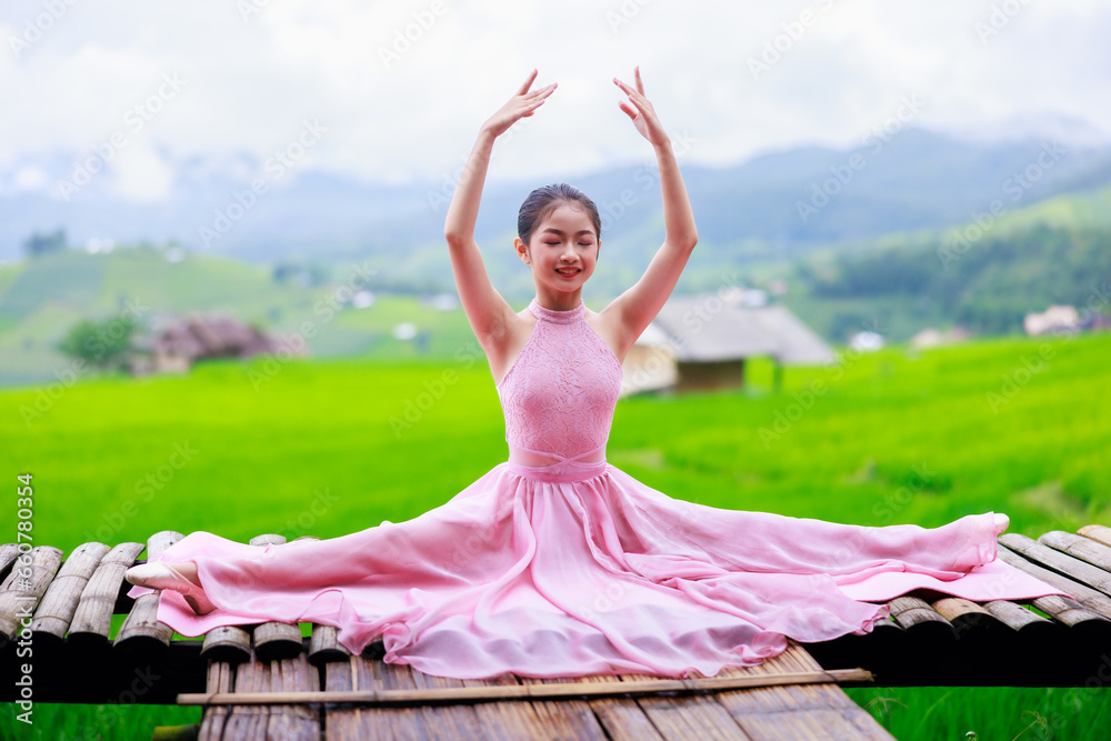 Fototapeta premium young girl ballerina in pink ballet dress dancing in pointe shoes in balcony at rice terraces Ban Pa Bong Piang. Ballerina sitting in beautiful ballet pos