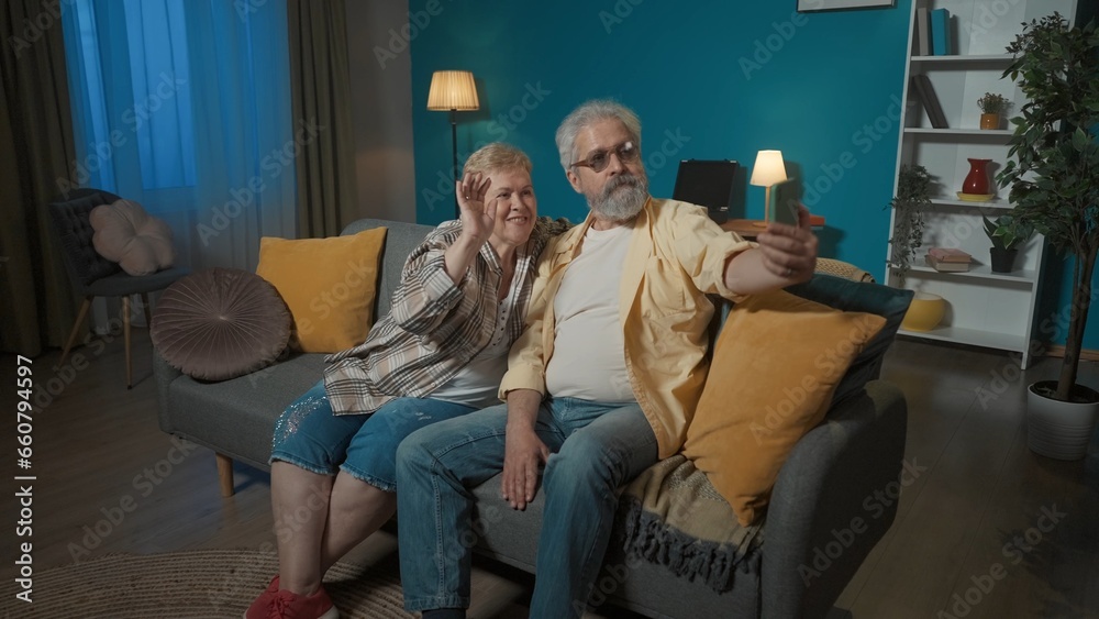 In the picture, an elderly couple is sitting on a sofa in a room. The man is holding a phone on his arm. The woman snuggled up against the man and both look at the phone. Demonstrate photo posing In the picture, an elderly couple is sitting on a sofa in a room. The man is holding a phone on his arm. The woman snuggled up against the man and both look at the phone. Demonstrate photo posing