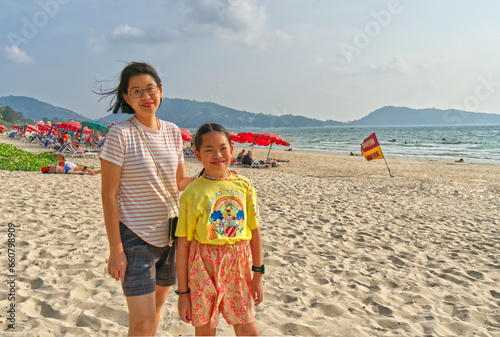 Portrait Asian middle-aged mother and little daughter in casual standing on Patong Beach of Phuket, Thailand, landscape image with space for copy.