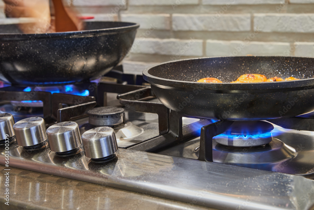 Frying pans on burner fire on gas stove with dish being prepared Frying pans on burner fire on gas stove with dish being prepared