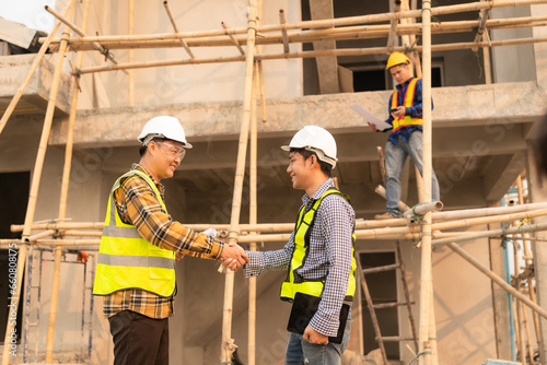 Architect and construction engineer holding hands while working for teamwork and cooperation concept after completing an agreement on construction site.