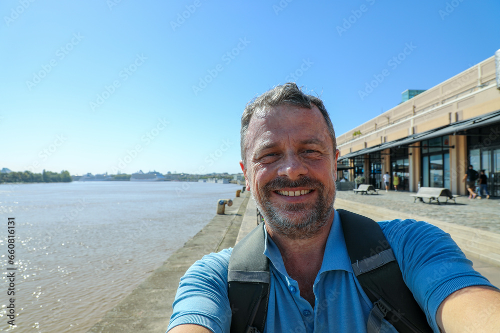 middle aged man taking a selfie phone on holidays bordeaux quay background - obrazy, fototapety, plakaty 