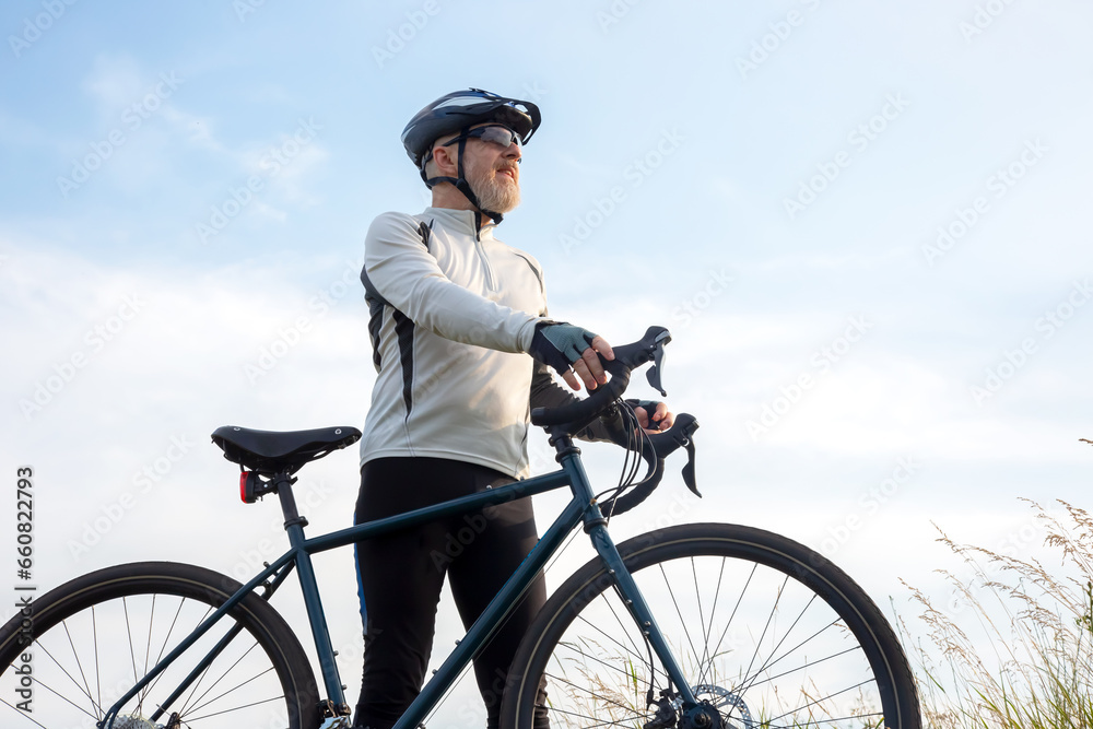 Obraz premium Bearded man cyclist stands with a bike against the blue sky. cycling and health hobbies