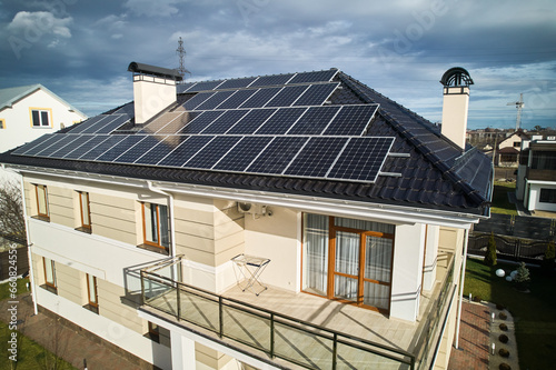 Home residence with solar panel system for generating electricity through photovoltaic effect. Aerial view of two-storey house with solar modules on roof. Ecological renewable energy sources concept. © anatoliy_gleb