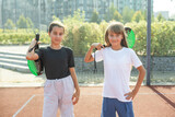 Kids and sports concept. Portrait of smiling girls posing outdoor on padel court with rackets and tennis balls