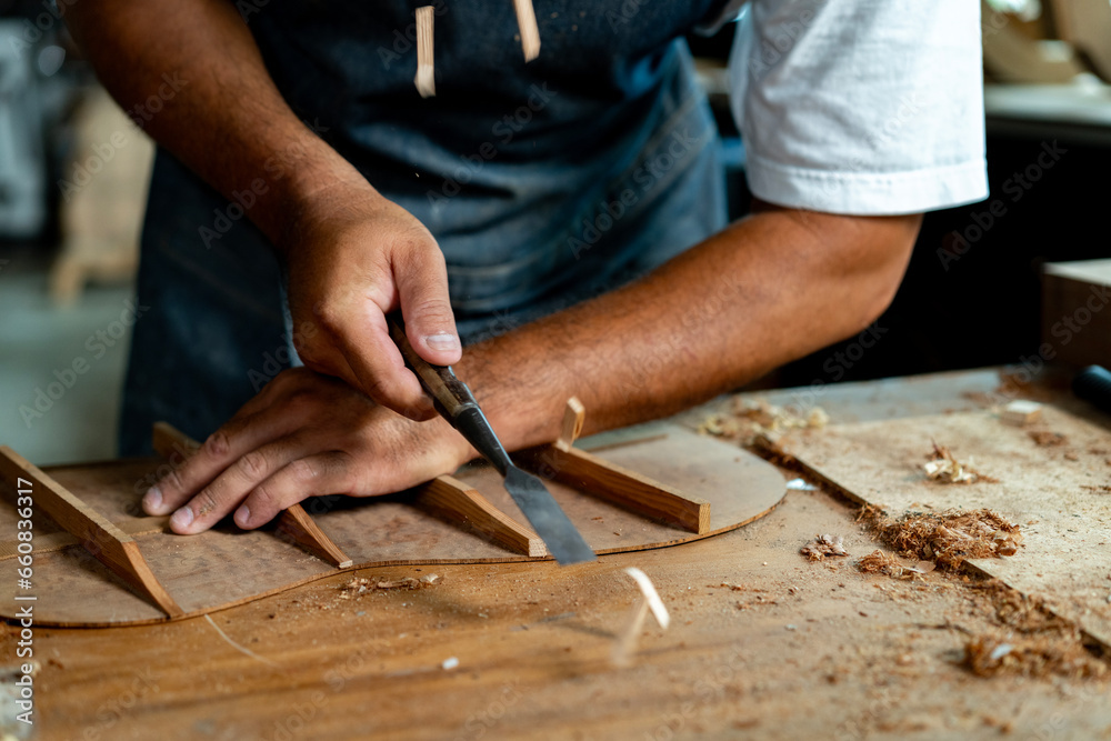Close-up of guitar luthier using chisel to shave bracing of acoustic guitar. Close-up of guitar luthier using chisel to shave bracing of acoustic guitar.