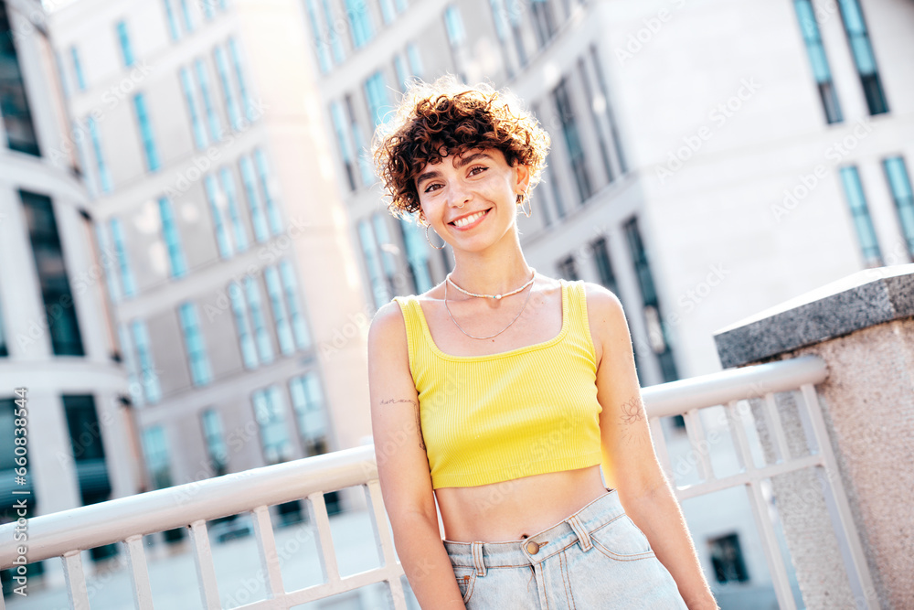 Young beautiful smiling hipster woman in trendy summer clothes. Carefree woman with curls hairstyle, posing on the street background at sunny day. Positive model outdoors. Cheerful and happy